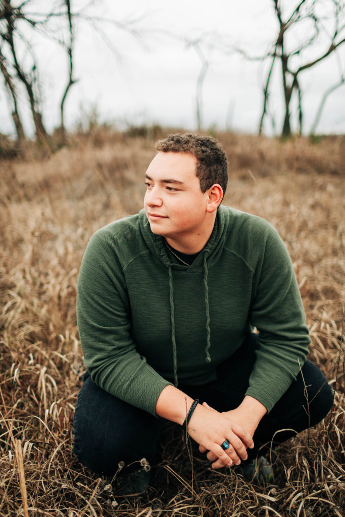 A senior sits in dry grass and gazes at the horizon