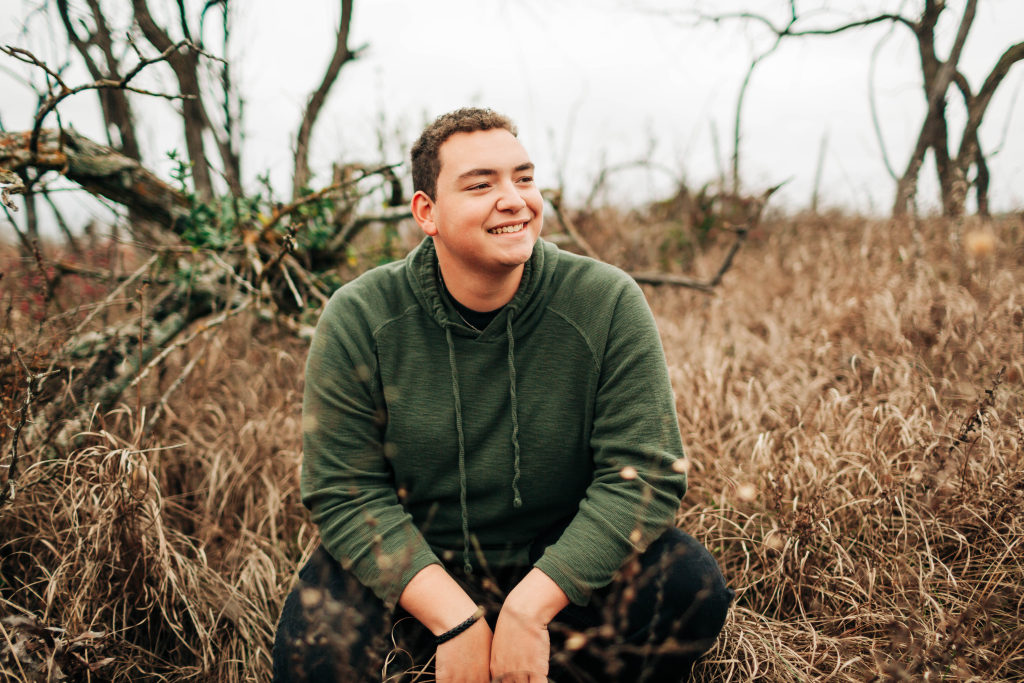 A senior sits in a country field and smiles