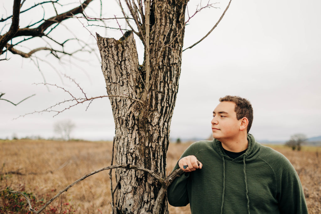 A senior gazes at the horizon with one arm on a tree in Harrison AR