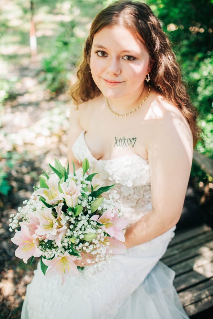 a bride sits on a rustic chair holding her bouquet in the shade
