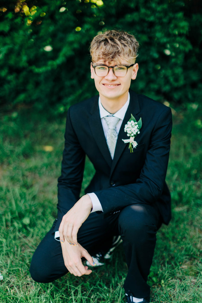 a groom crouches on a knee while looking at the camera