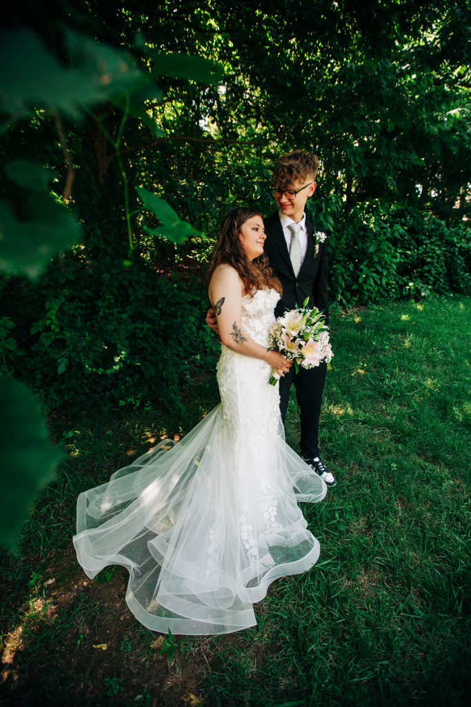 a bride and groom cuddle in the shadow of a forest