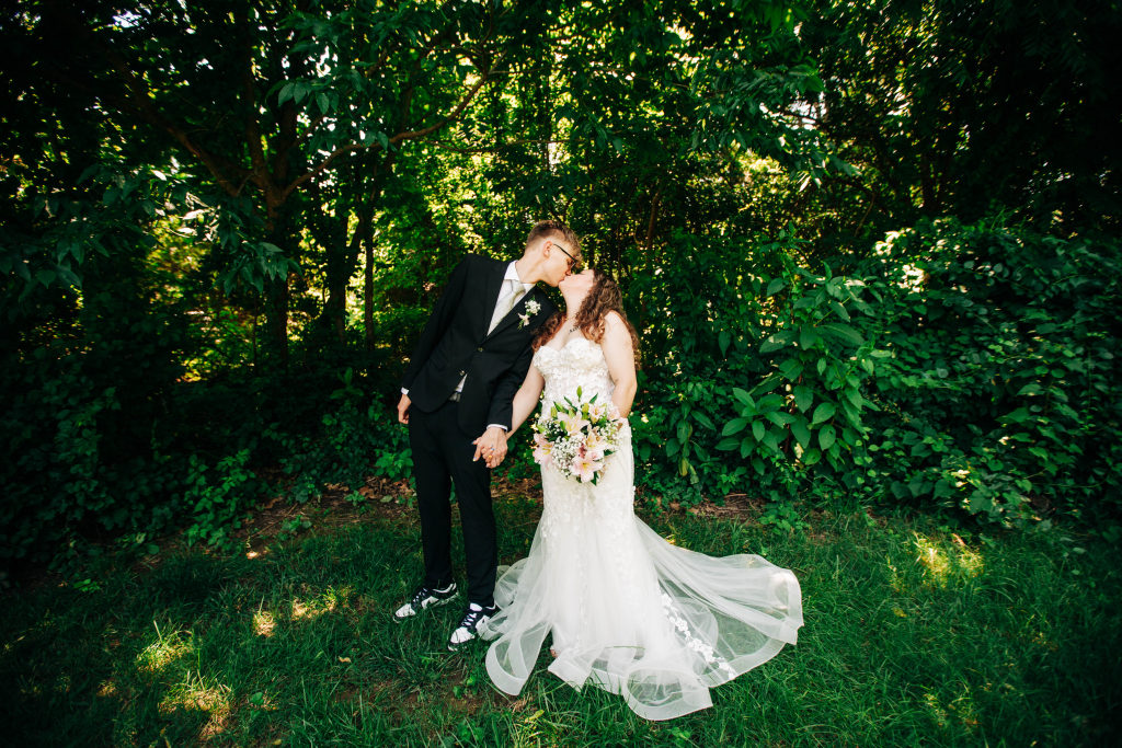 a bride and groom share a kiss while standing in shaded grass on their elopement day