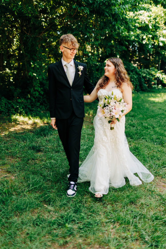 a bride and groom walk together in the shade on green grass