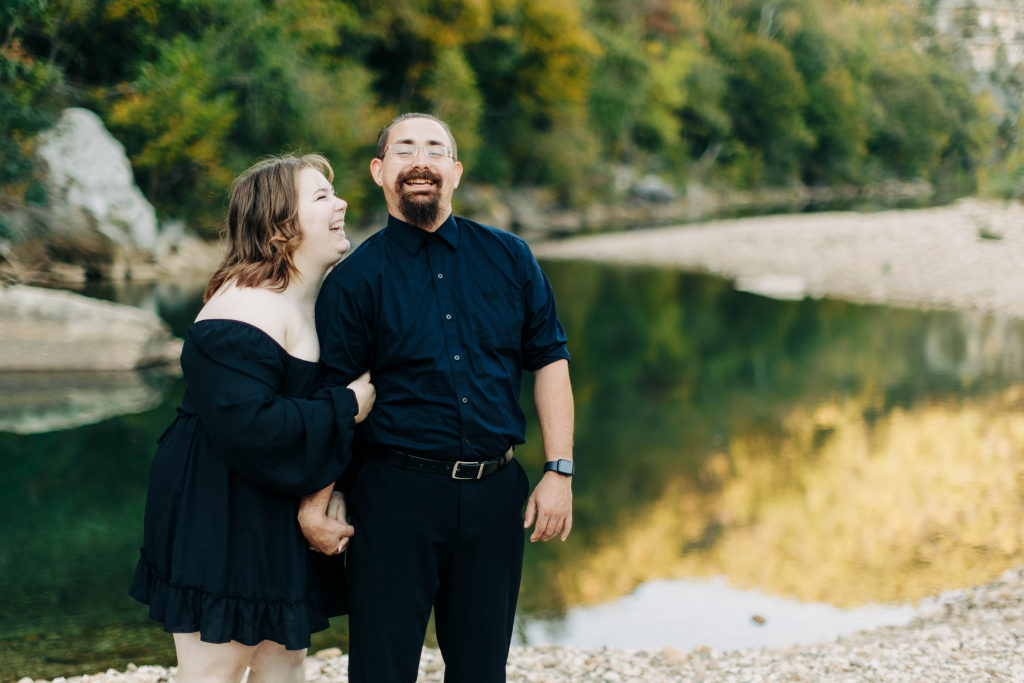 a couple hold each other in the Ozarks and laugh with a mirror-like pool in the background