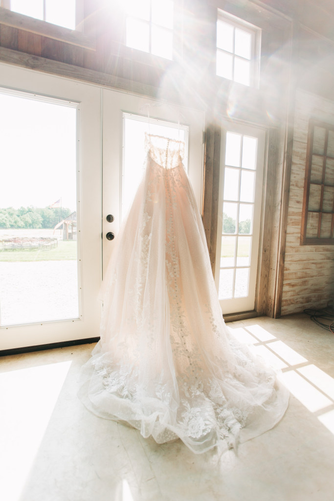 bride's dress hangs from a window with beautiful sunlight streaming in