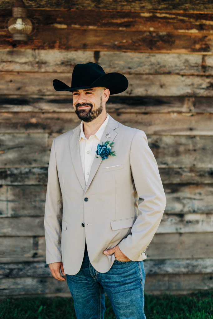 groom poses with one hand in a pocket, wearing his stetson hat