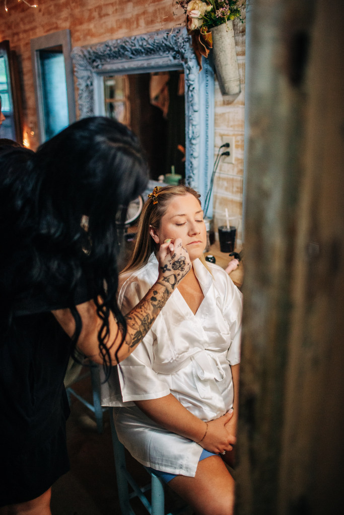 bride gets ready for her wedding by having her makeup done while sitting