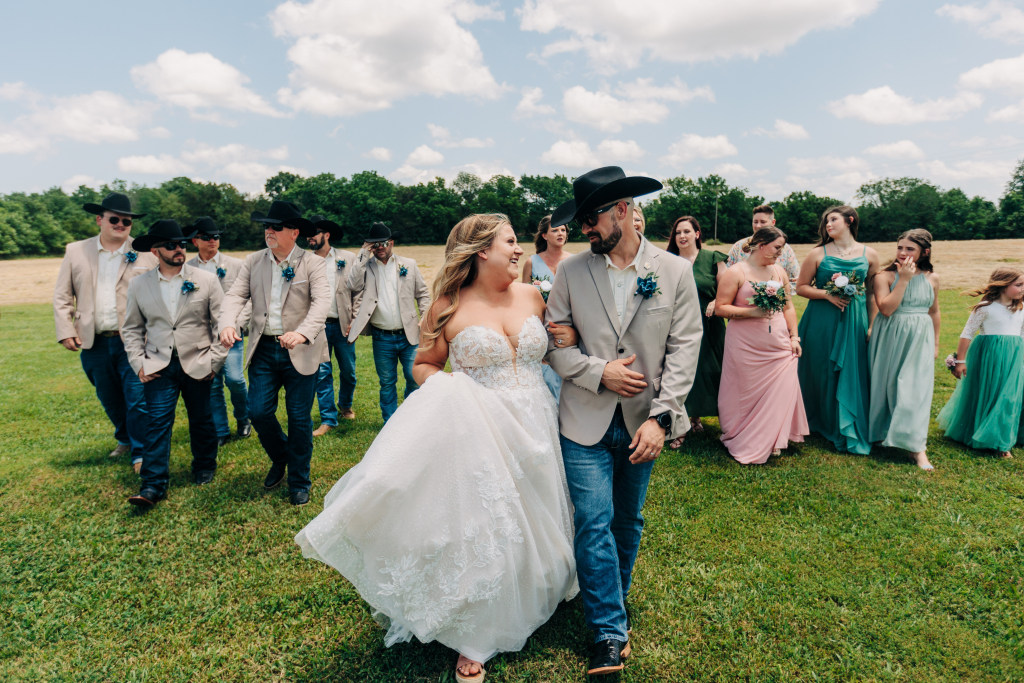 full bridal party walk in a field while talking together and laughing