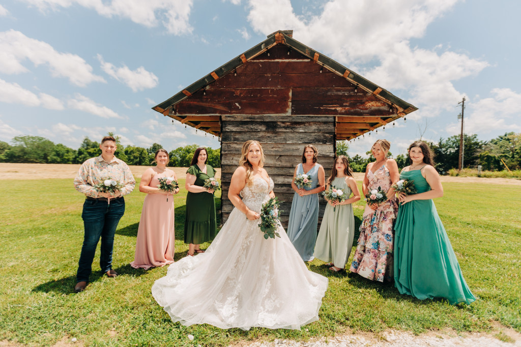 bridesmaids stand in a circle around the bride in front of a rustic cabin