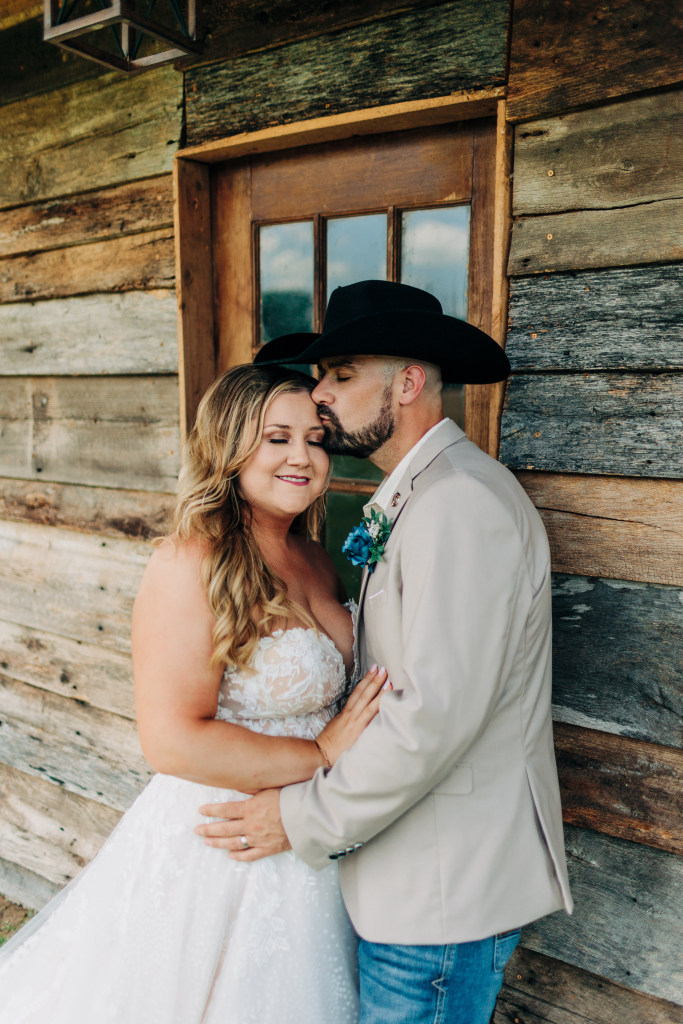 groom kisses the bride on her forehead next to a rustic cabin