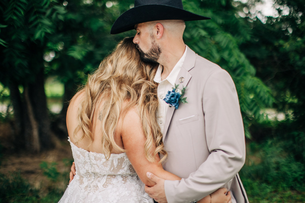groom kisses brides hair from behind in the shade of a tall tree