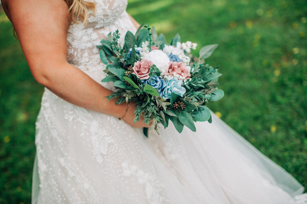 bride holds her bouquet against her dress in the shade of a tall tree