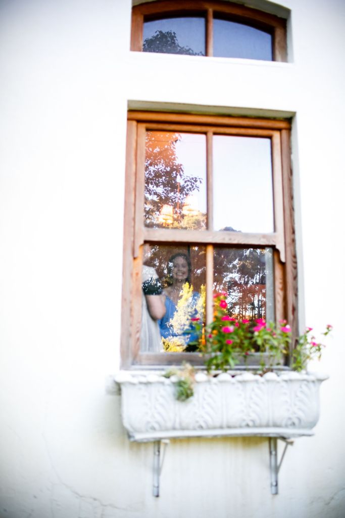 bride shows her excitement as she look out from behind a beautiful wooden window on a white-washed building