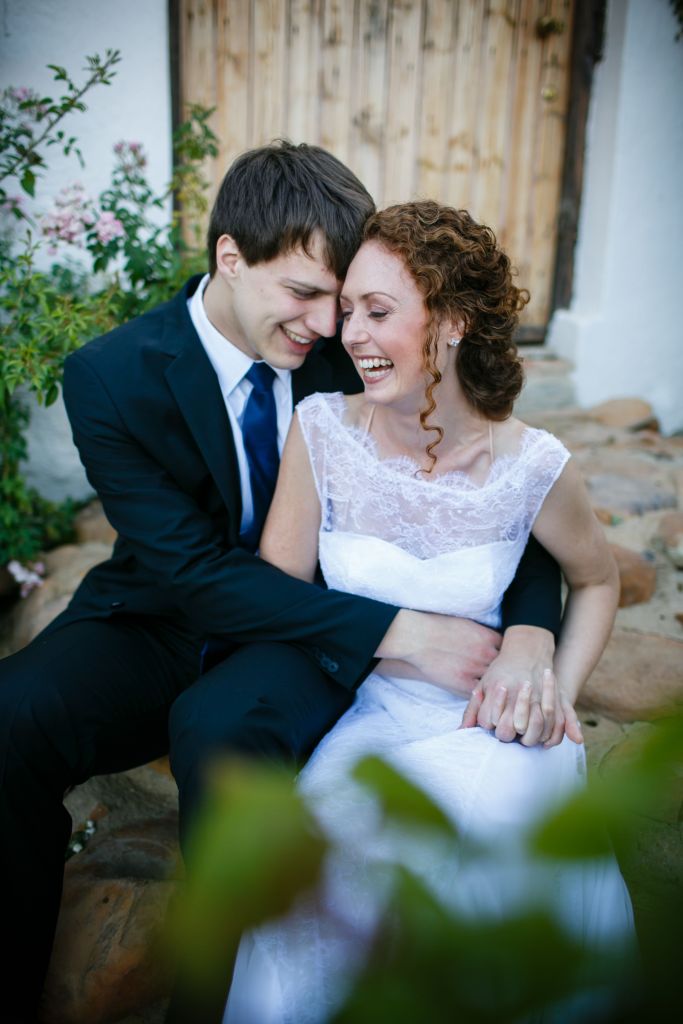bride and groom laugh together on rustic stone stairs with a wooden door in the background