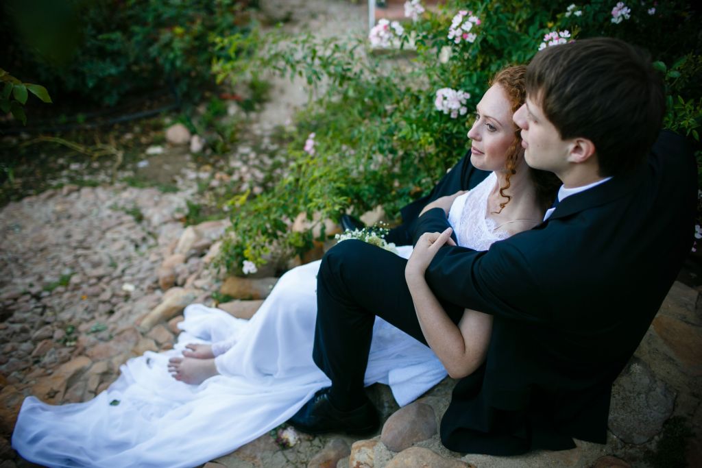 bride and groom embrace leisurely on rocky stairs next to rose bushes