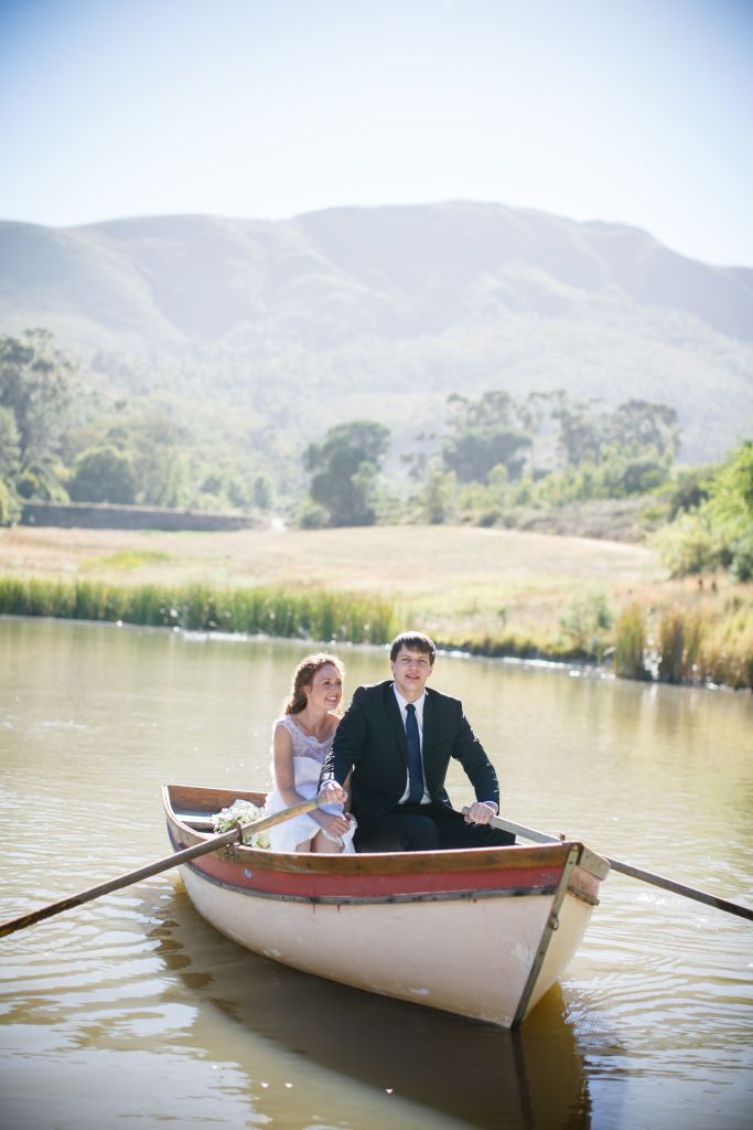 bride and groom row out onto a calm lake with reeds and a mountain in the background