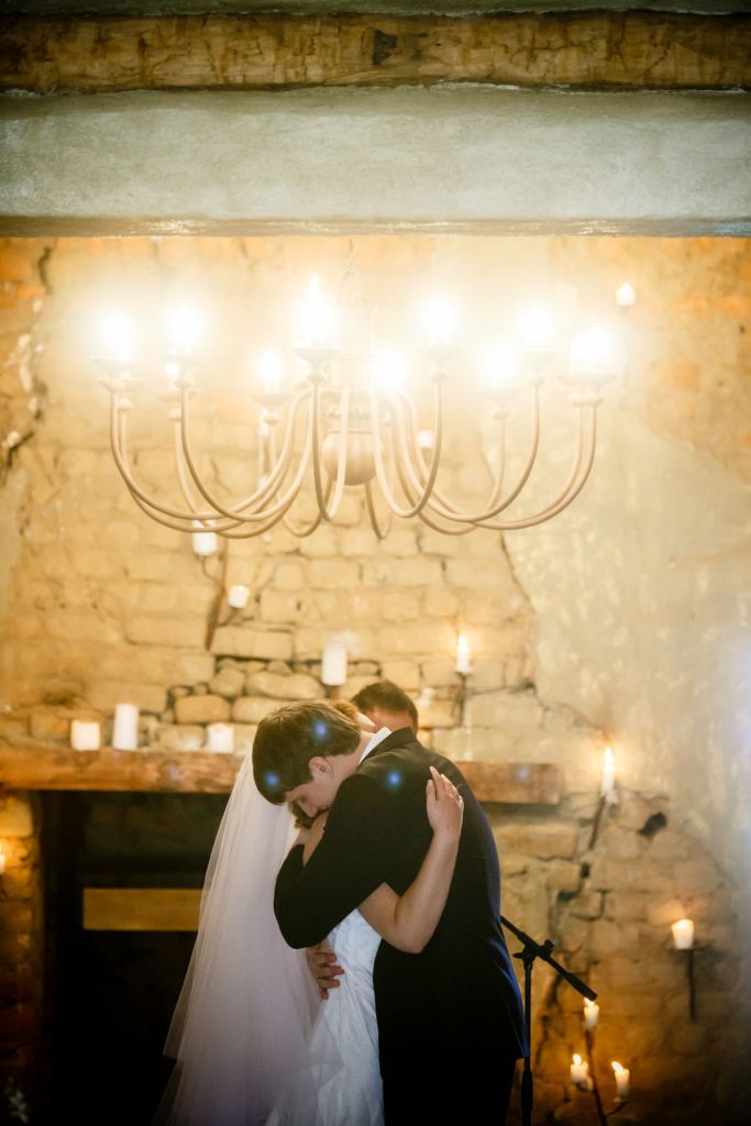 bride and groom embrace in a rustic setting under a copper chandelier after saying their wedding vows