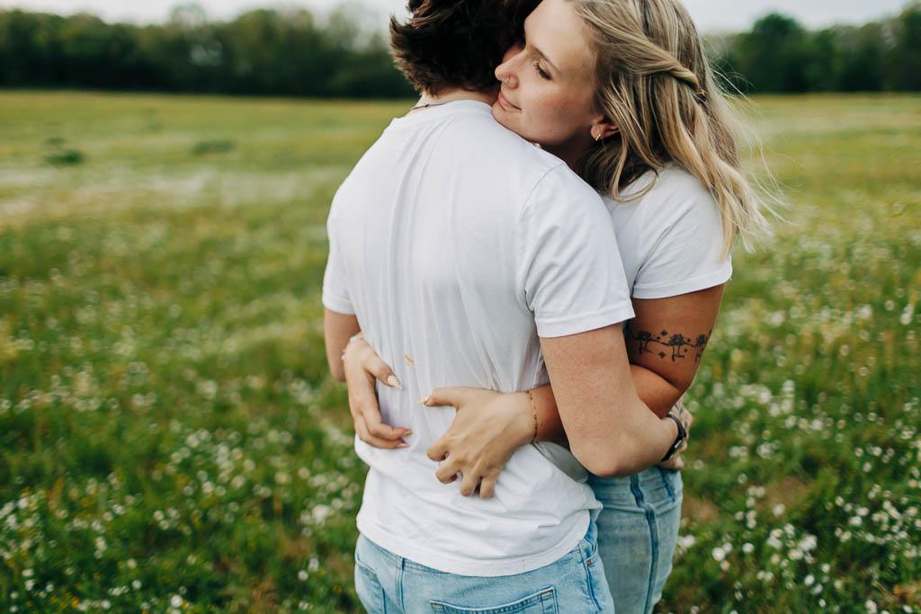 young couple embrace in a green field full of flowers near Harrison AR