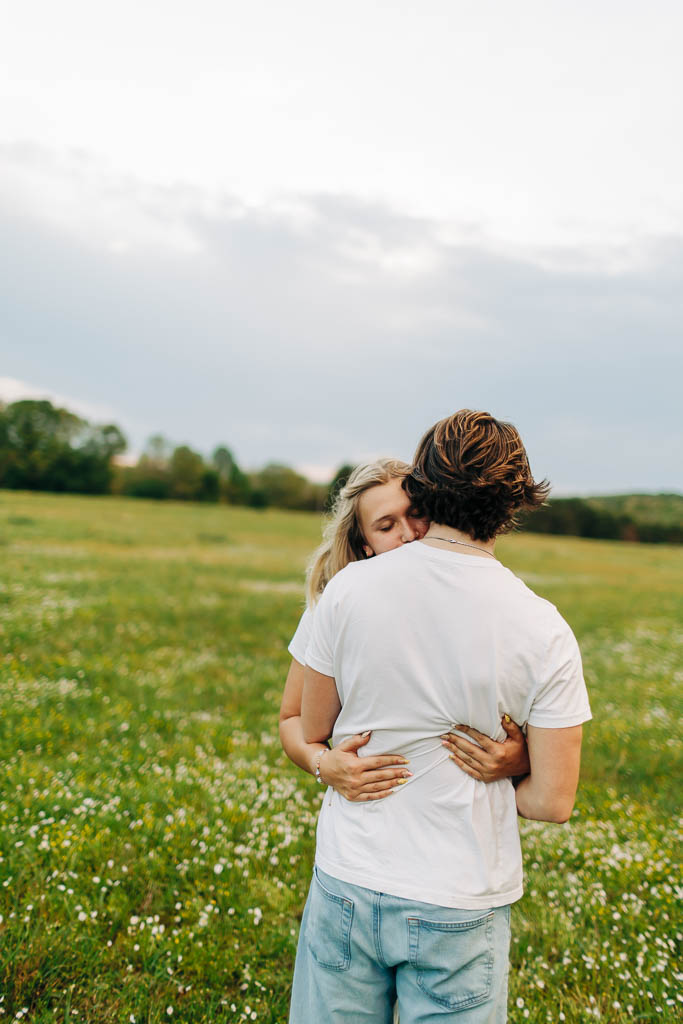 guy and girl relax into each others embrace while standing in a green flowery field