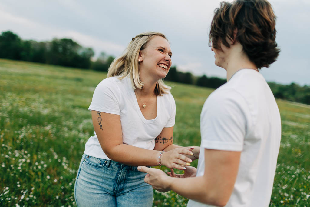 a guy and girl playfully react to each other in a flowery grass field