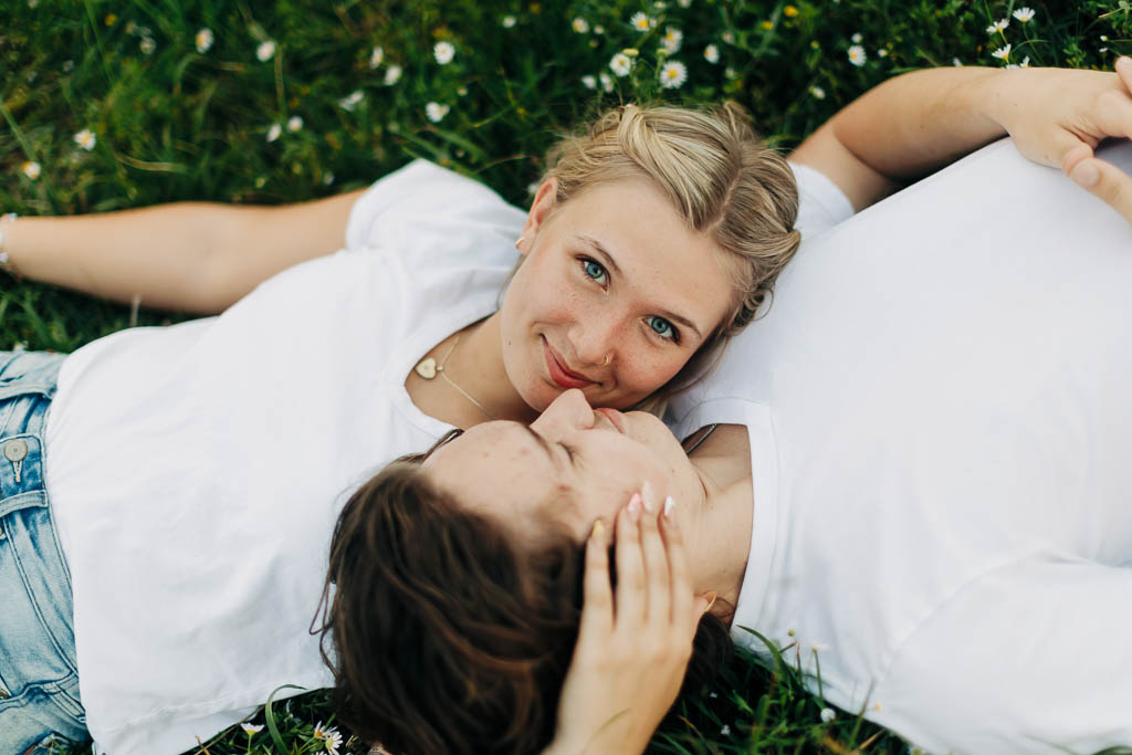 a guy and girl lie back with their heads nestled together in a country flower field