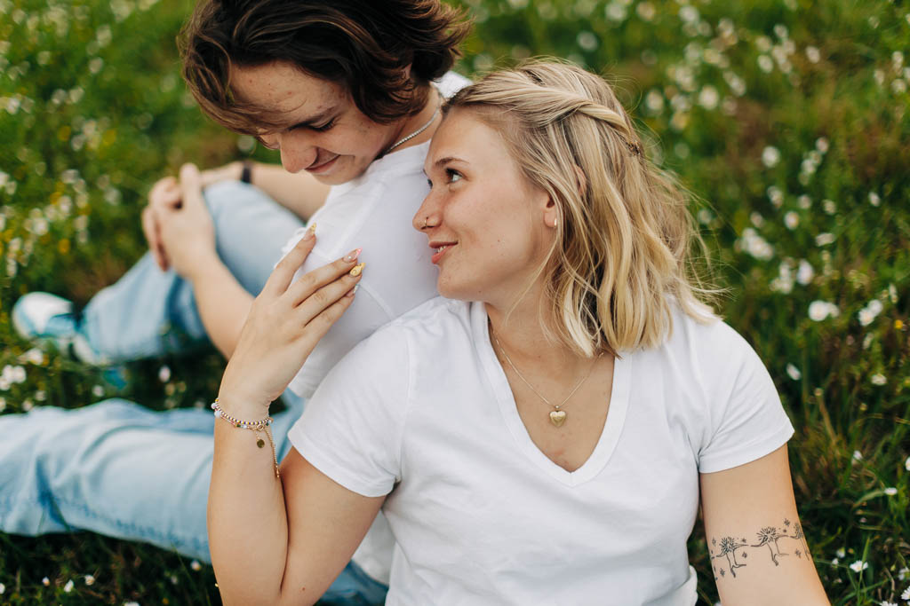 a girl smiles while touching her boyfriend's shoulder while leaning into his back
